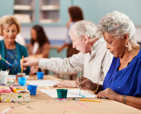 A group of people sitting at tables with paint and pencils.