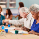 A group of people sitting at tables with paint and pencils.