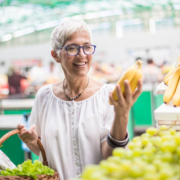 A woman holding a banana in front of some fruit.