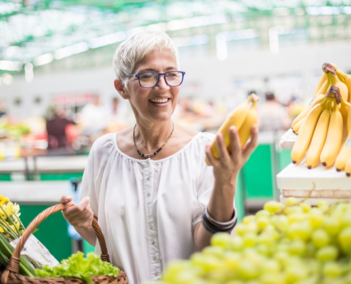 A woman holding a banana in front of some fruit.