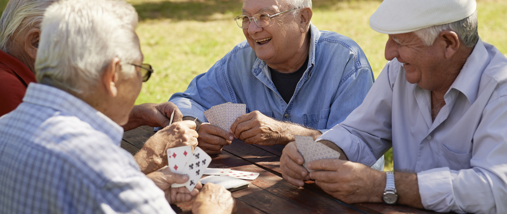 Three older men playing cards at a picnic table.