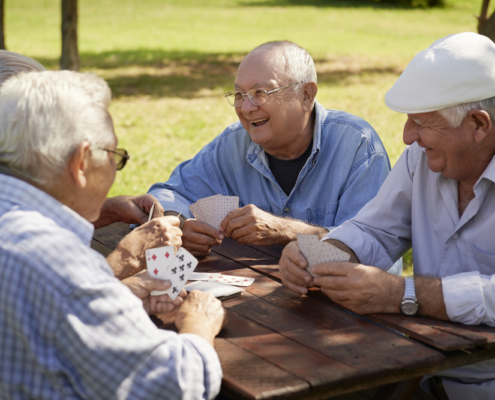 Three older men playing cards at a picnic table.